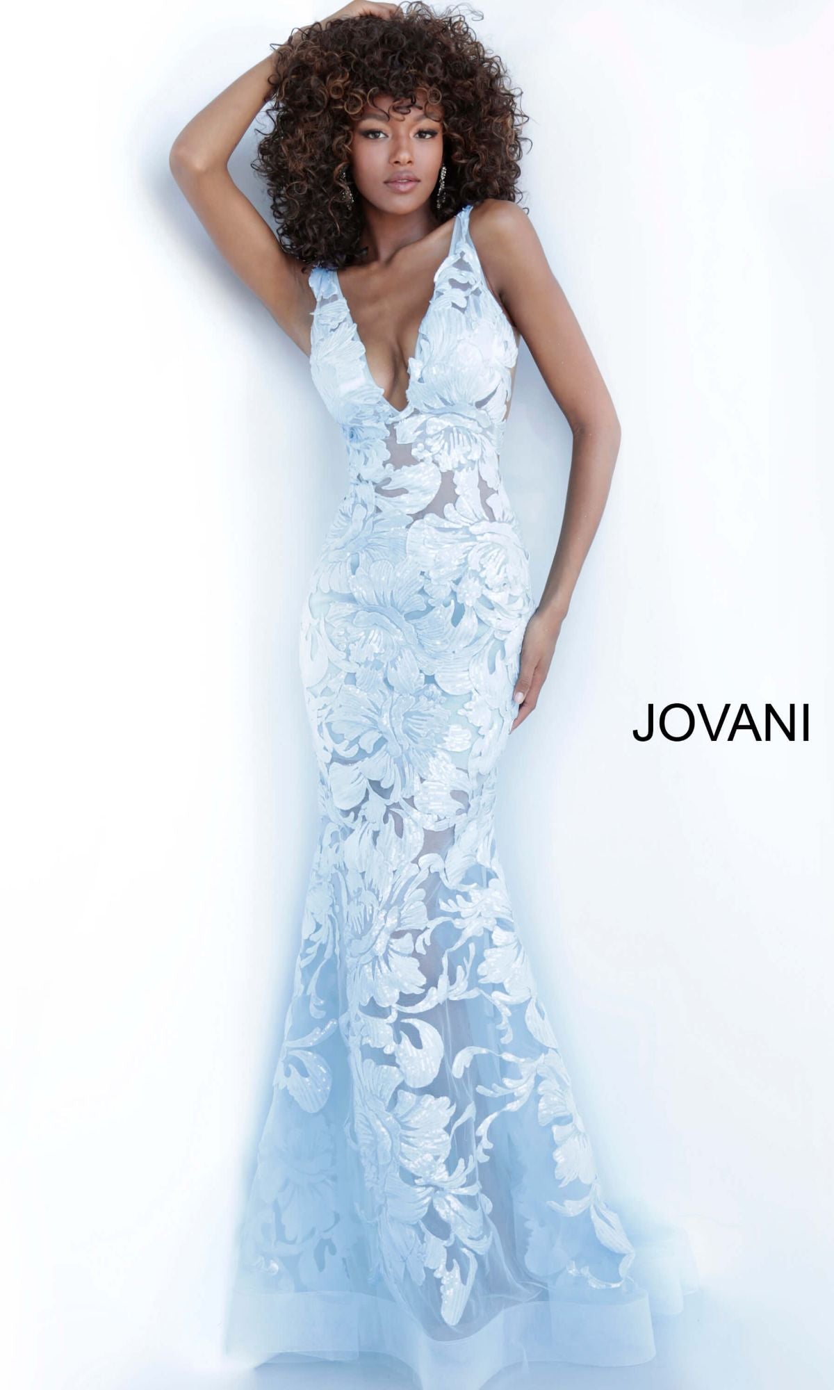 A woman poses in a Jovani Embroidered Long Prom Dress with Sequins featuring pale blue floral embroidery, a deep V-neck, and flared hem against a white background.